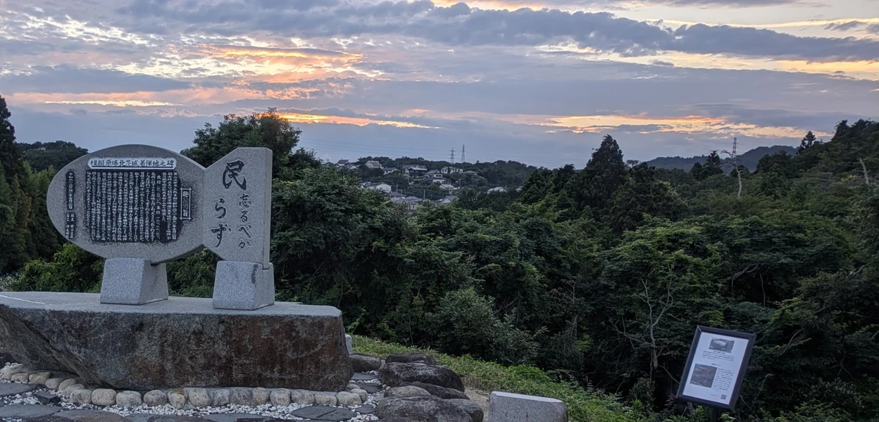 夕空を背景に立つ、模擬原爆の形をした記念碑(提供写真をトリミング・色調整)